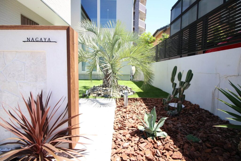 リゾート感のある洋風オシャレ外構。白い門柱とウッドチップを組み合わせた植栽で高級感の演出。