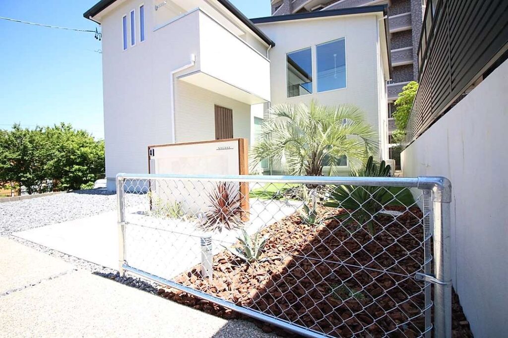 リゾート感のある洋風オシャレ外構。白い門柱とウッドチップを組み合わせた植栽で高級感の演出。